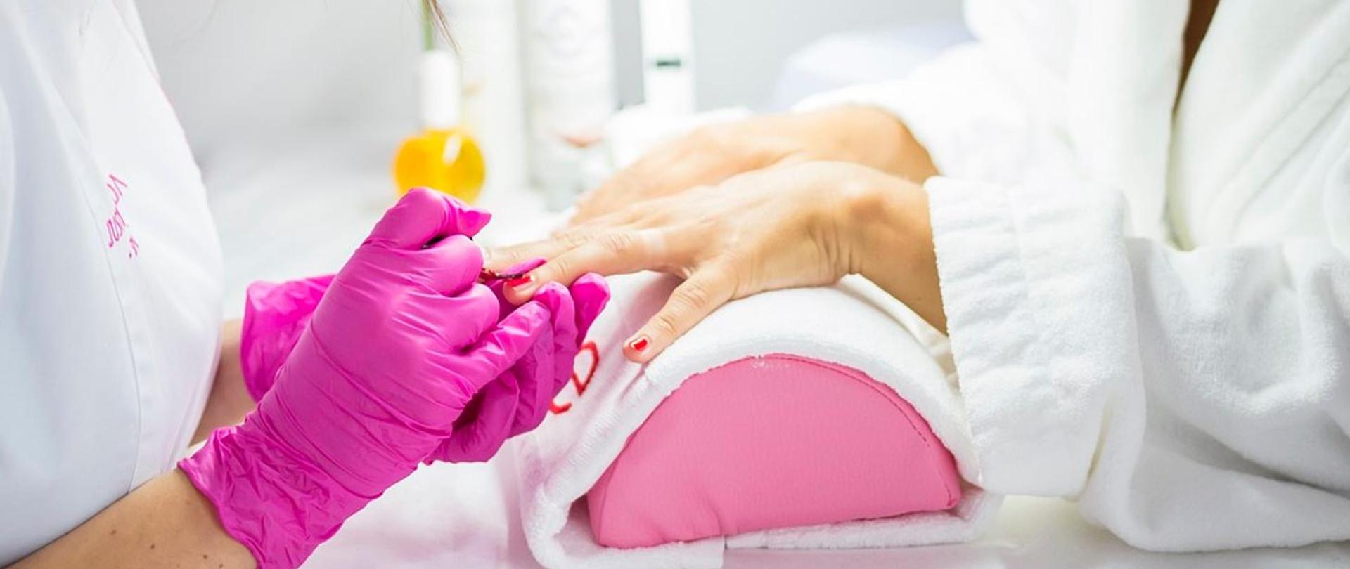 dłonie kosmetyczki i klientki w czasie zabiegu manicure
