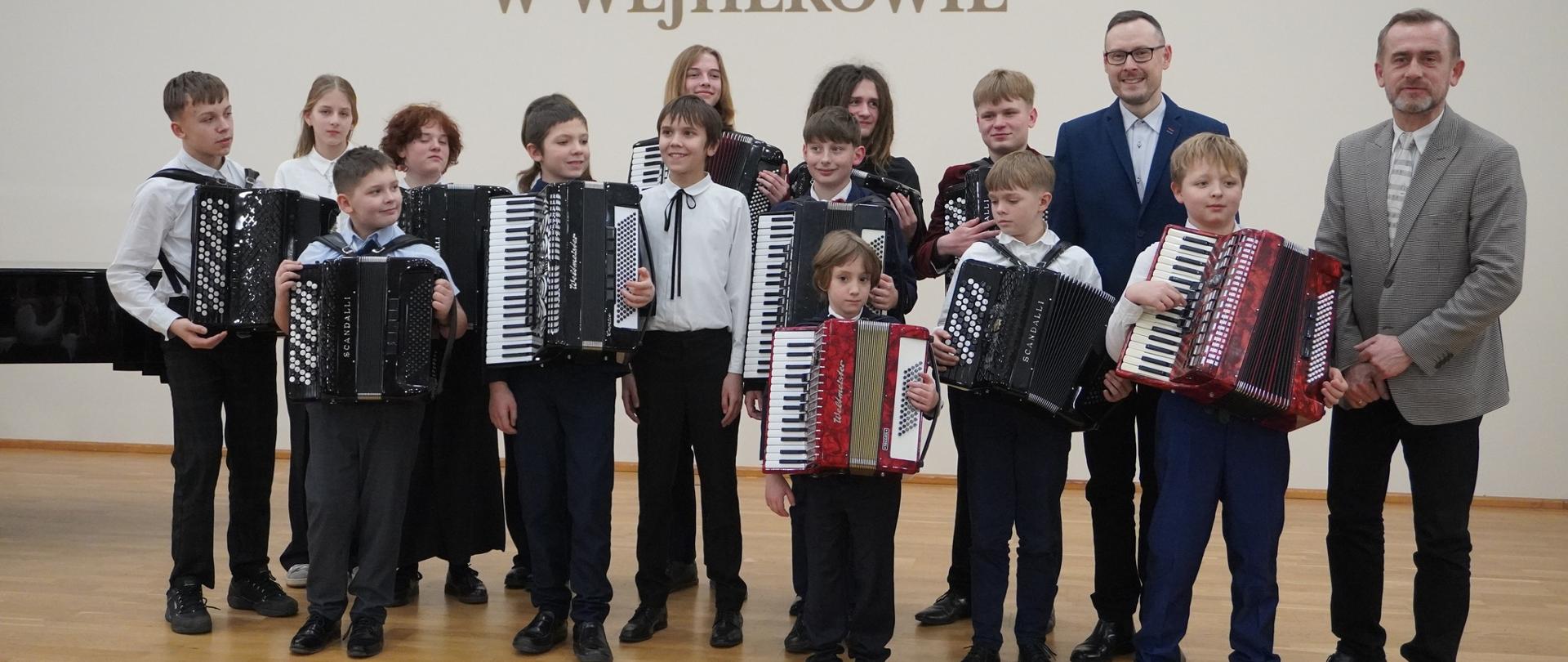 Na sali koncertowej pozują uczniowie z akordeonami. Na zdjęciu również nauczyciele - Ryszard Borysionek i Andrzej Formela.