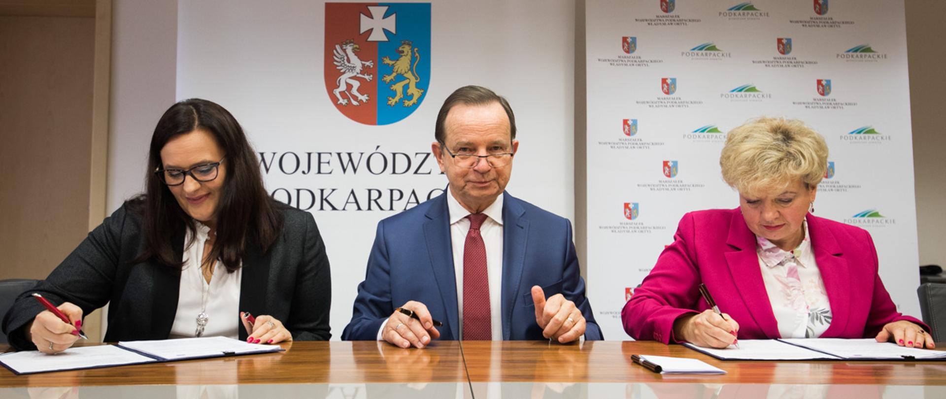 Na tle roll-upu województwa podkarpackiego przy stole siedzą od lewej: wiceminister Małgorzata Jarosińska-Jedynak, marszałek Władek Ortyl oraz wicemarszałek Ewa Draus