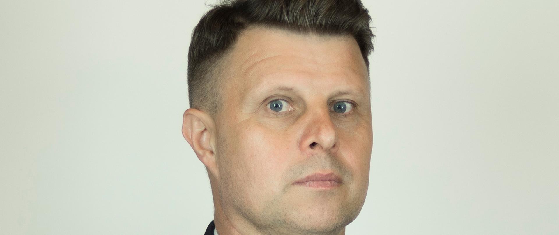 Zdjęcie przedstawia Komendanta Powiatowego PSP w Górze. Jest to portret w ciemnym mundurze strażackim na jasnoszarym tle. Na mundurze widoczne są oznaczenia stopnia, odznaczenia oraz tabliczka z nazwiskiem „K. Panocha”. Na lewym ramieniu znajduje się ozdobny złoty sznur.”