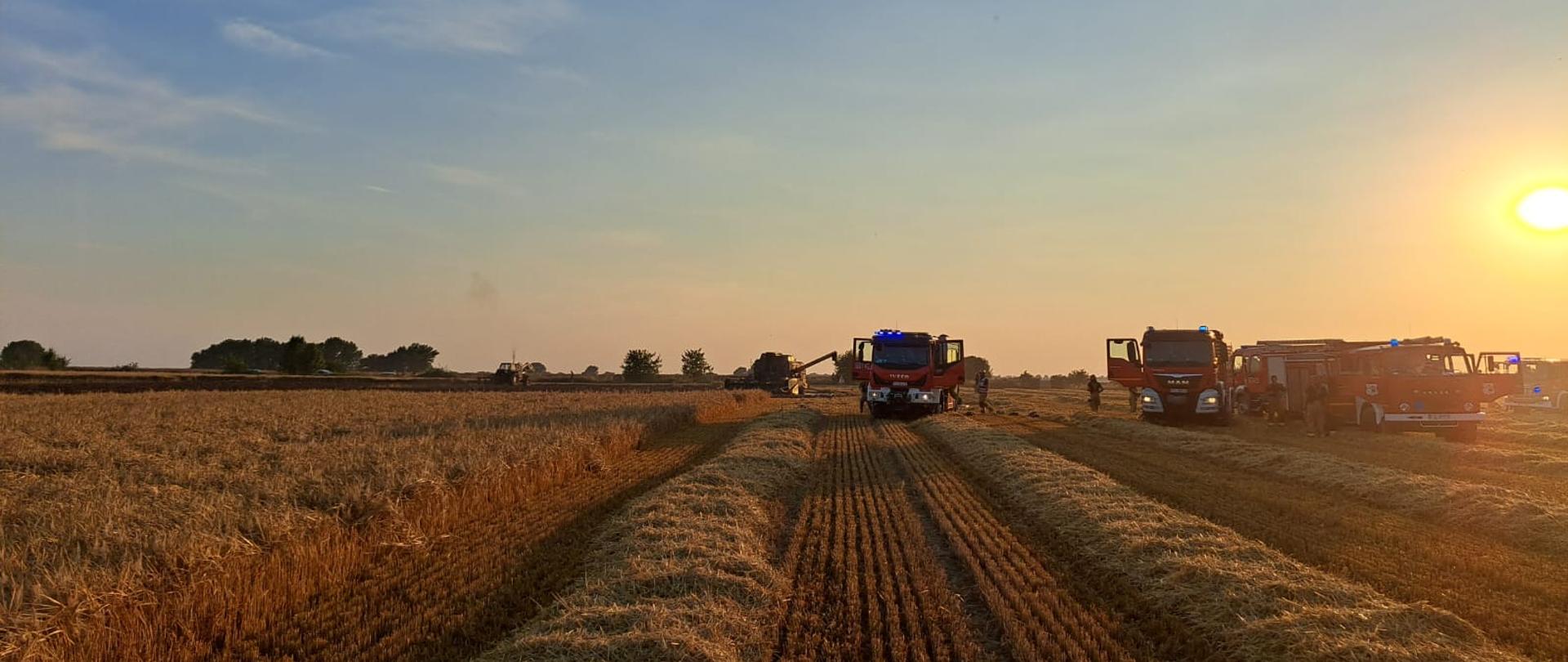 Na zdjęciu samochody strażacki na polu oraz spalony kombajn