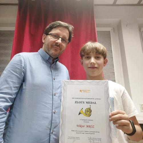 Chłopiec trzyma dyplom, obok niego stoi mężczyzna.