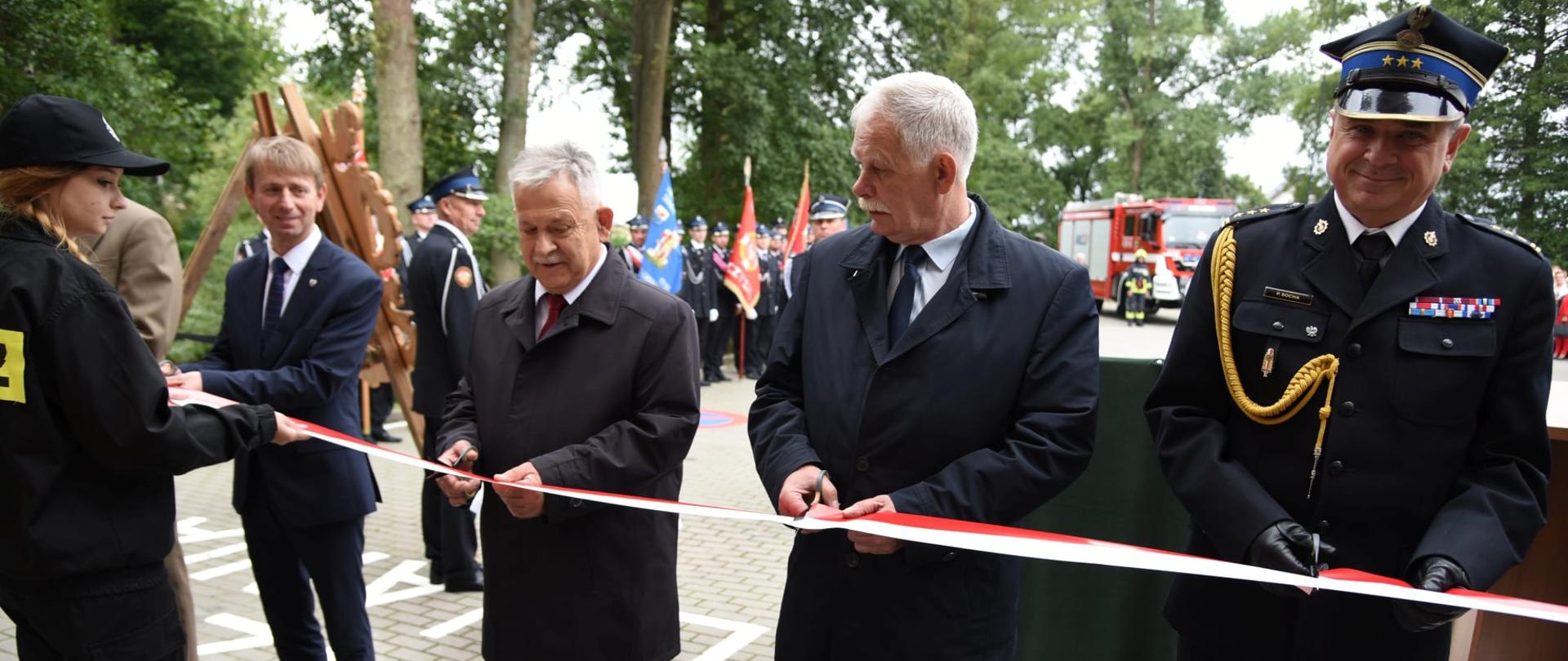 Uroczyste przecięcie wstęgi do nowej remizy. Biało czerwoną wstęgę przecinają kolejno od prawej: Pomorski Komendant Wojewódzki PSP st. bryg. Piotr Socha, Wicewojewoda Pomorski pan Mariusz Łuczyk, Poseł na Sejm RP pan Aleksander Mrówczyński, Burmistrz Brus pan Witold Ossowski. W tle znajdują się poczty sztandarowe oraz nowy wóz strażacki należący do OSP Leśno.