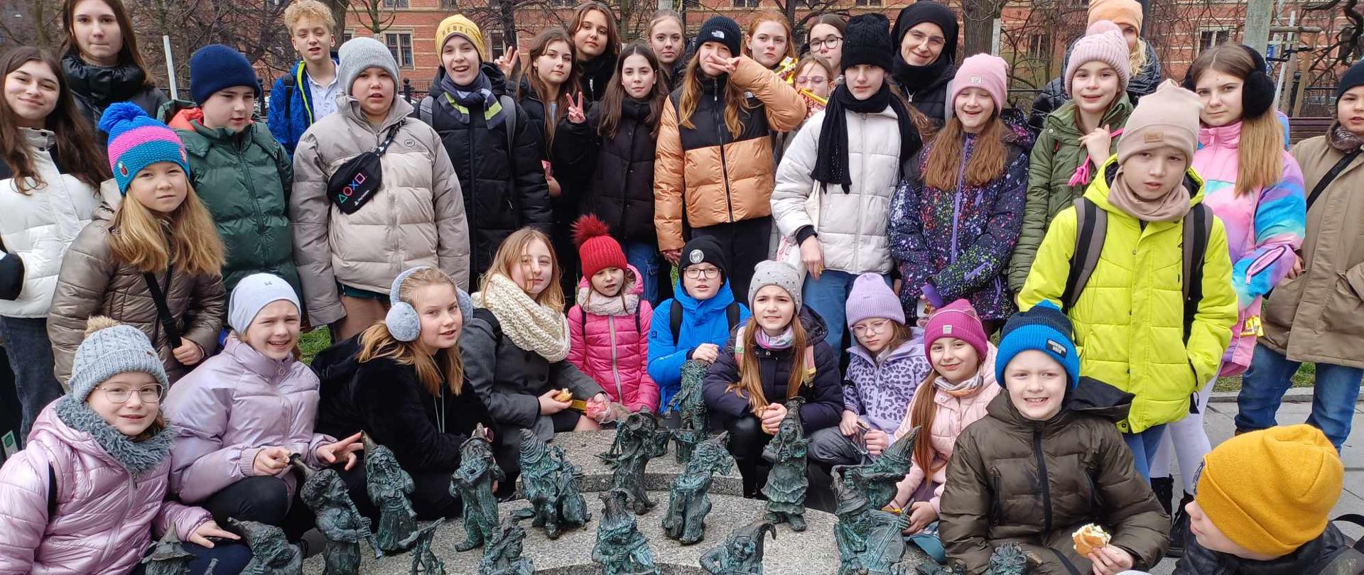 Grupa uczniów z opiekunami - przed nimi figurki krasnali z instrumentami