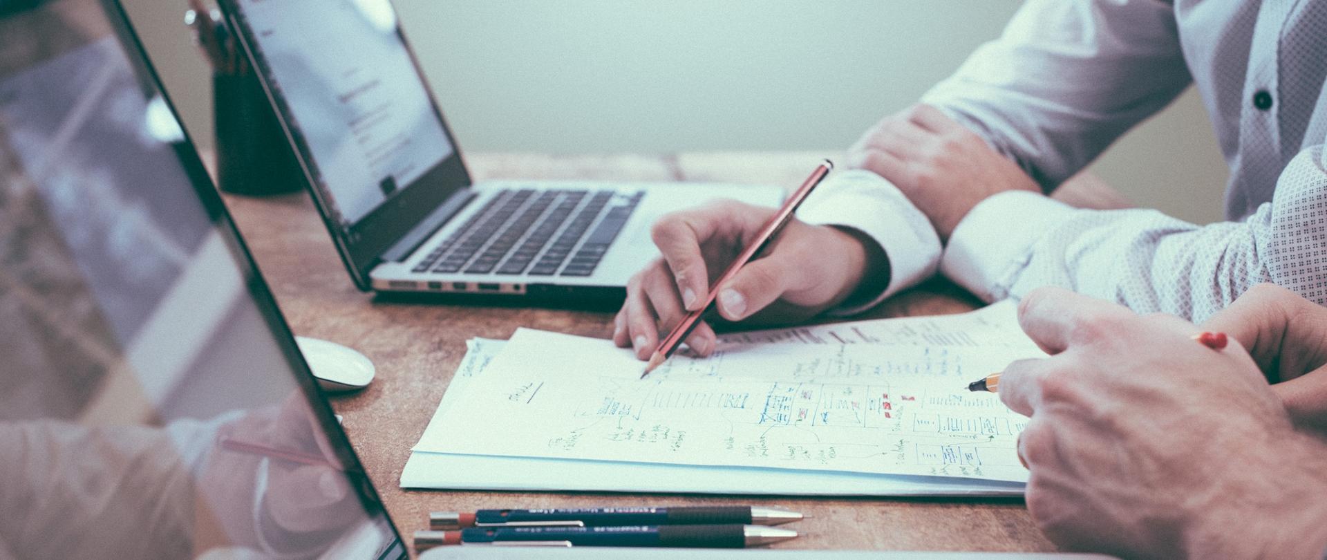 Zdjęcie - kilka osób siedzi przy biurku przed laptopami.