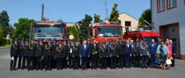 strażacy druhowie i inni uczestnicy uroczystości pozują do zdjęcia na tle samochodów pożarniczych z prawej strony widać bramę garażową z nr 6