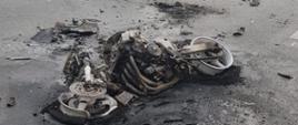 Na zdjęciu widać spalony motocykl, który znajduje się na asfaltowej drodze. Jest widno.