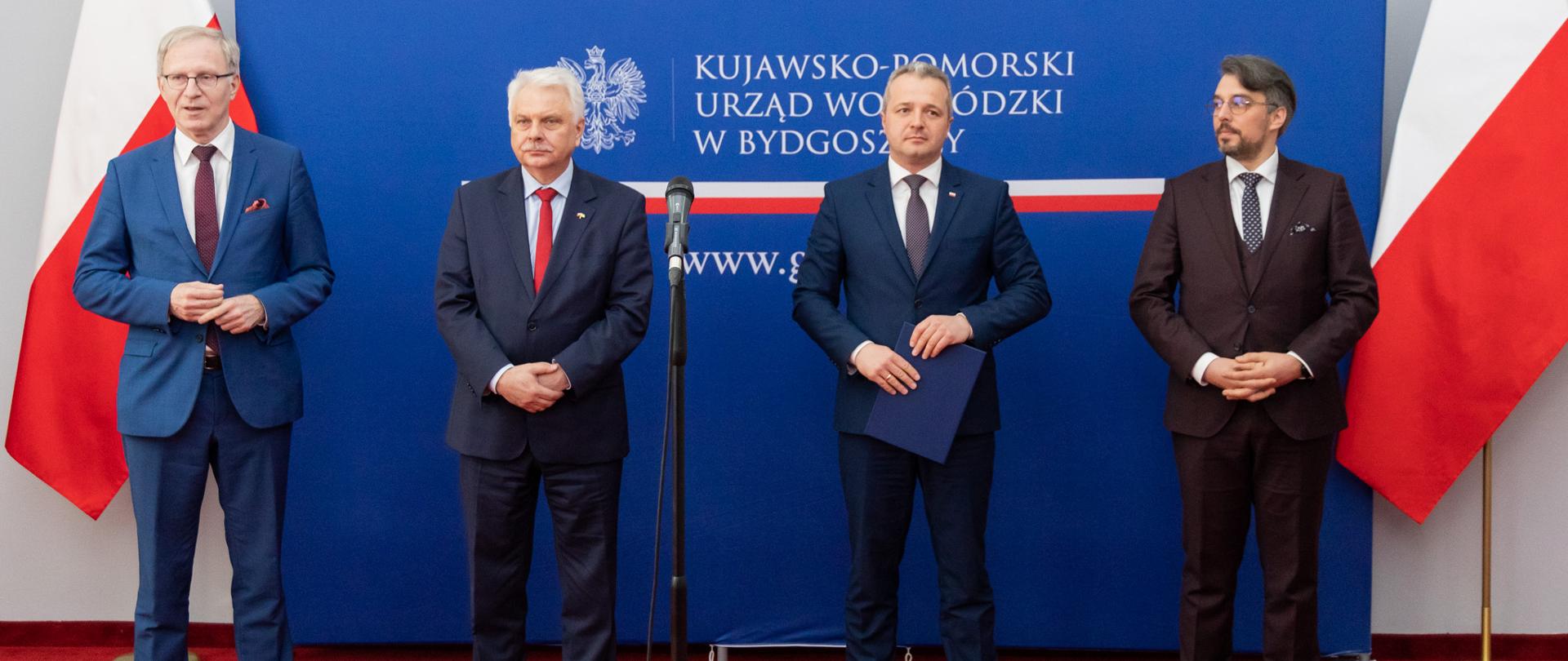 Czterech mężczyzn stojących na tle granatowej ścianki