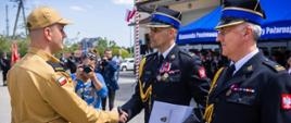 Na zdjęciu widoczni komendant powiatowy Państwowej Straży Pożarnej w Gorlicach z zastępcą wręczający strażakowi awans na wyższy stopień służbowy. Komendanci w galowych granatowych mundurach i w czapkach rogatywce. Strażak odbierający awans w ubraniu służbowym i czapce z daszkiem koloru piaskowego.
