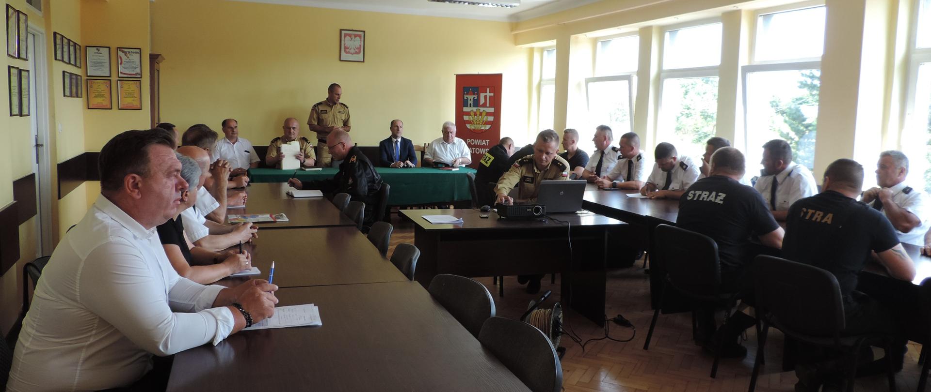 Zdjęcie przedstawia strażaków na sali szkoleniowej siedzących przy stołach.