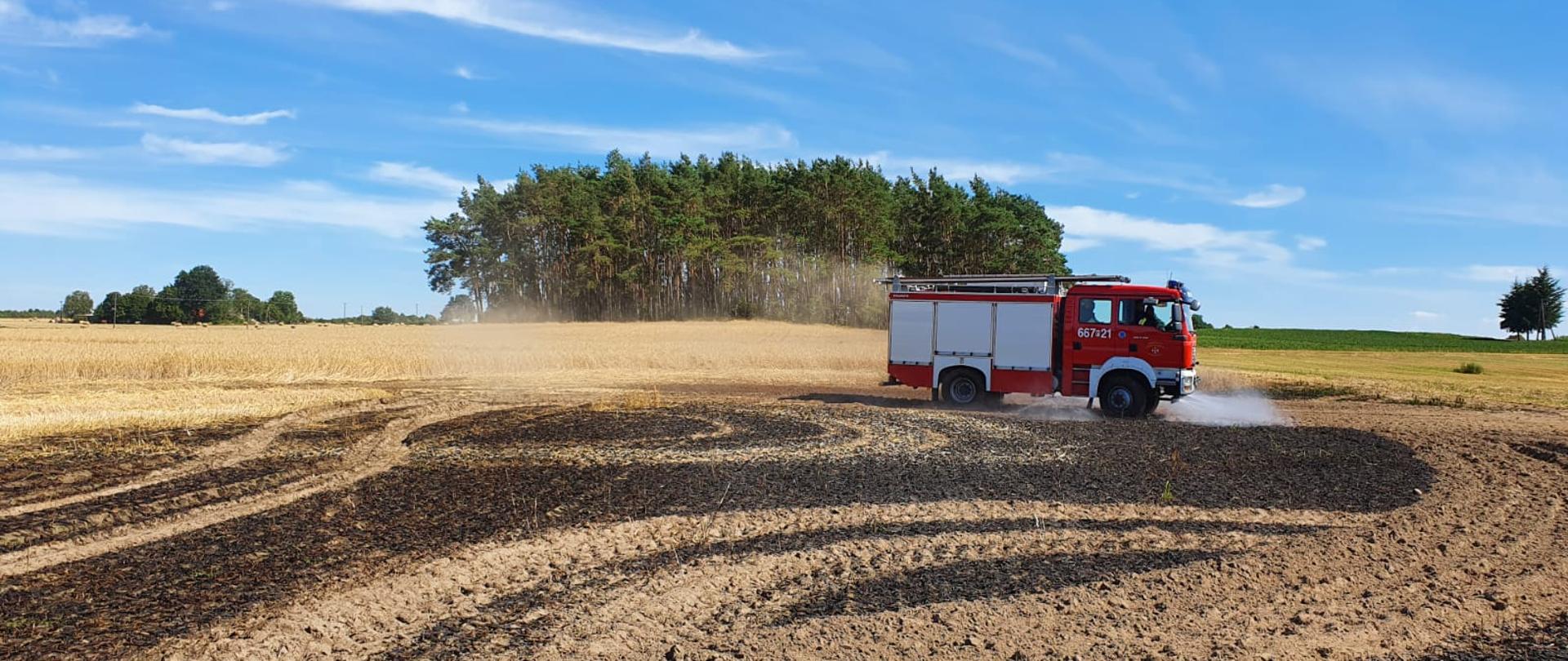 widok spalonego pola po,którym jeździ samochód strażacki