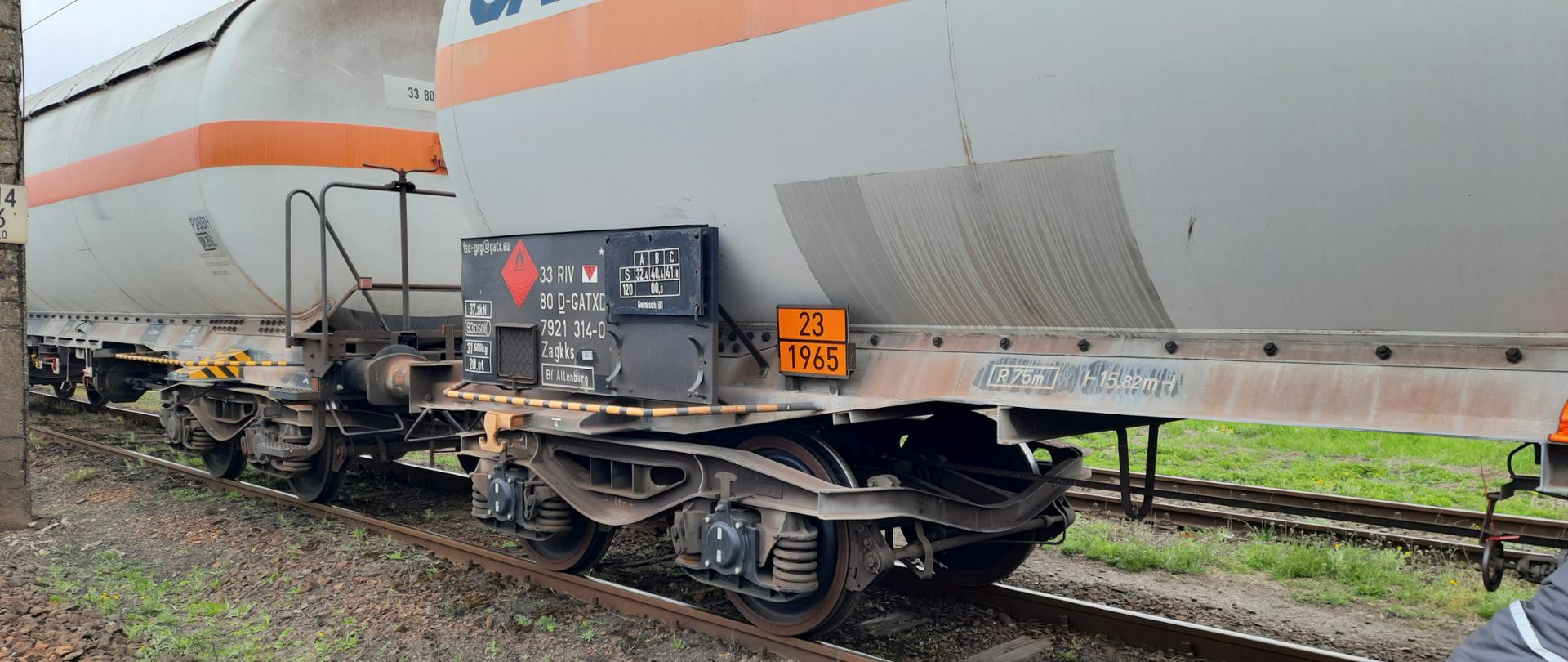 Dwie cysterny kolejowego koloru szarego stojące na torach, widoczna tabliczka znamionowa cysterny i numery ONZ gazu