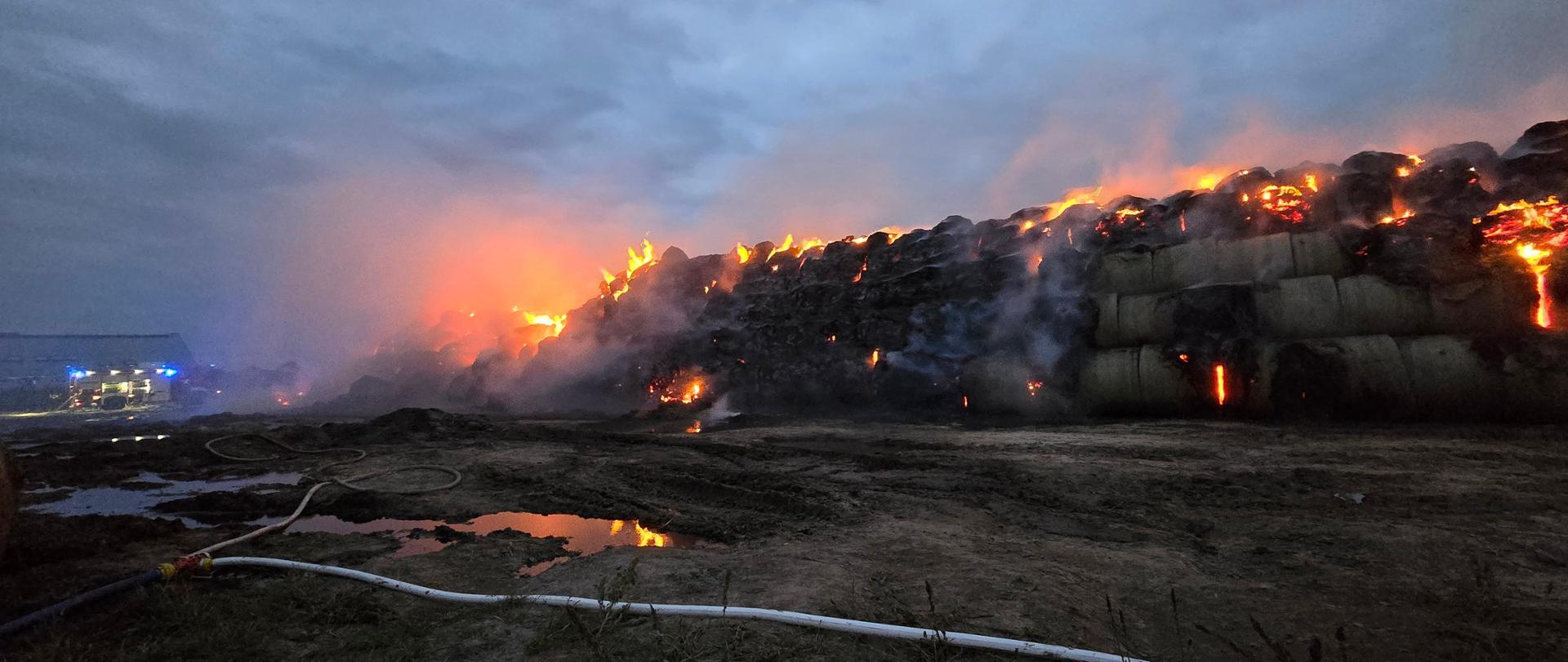 zdjęcie przedstawia pojazdy pożarnicze na tle palącego się stogu siana