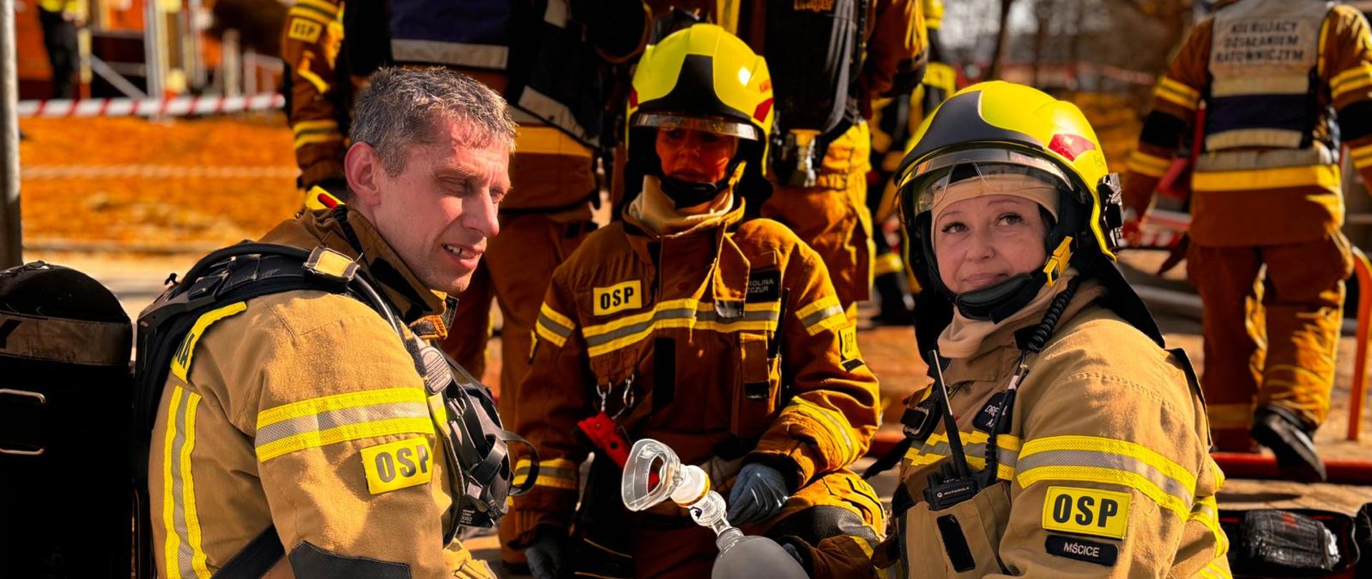 Strażacy w umundurowaniu ochronnym przygotowują sprzęt medyczny do udzielania pomocy poszkodowanemu.