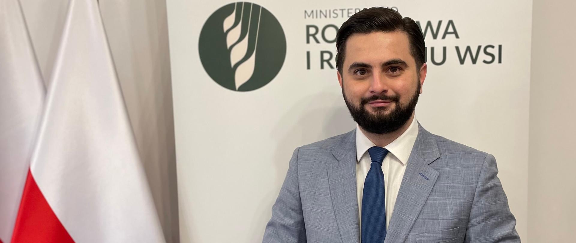 Minister Norbert Kaczmarczyk na tle flagi Polski