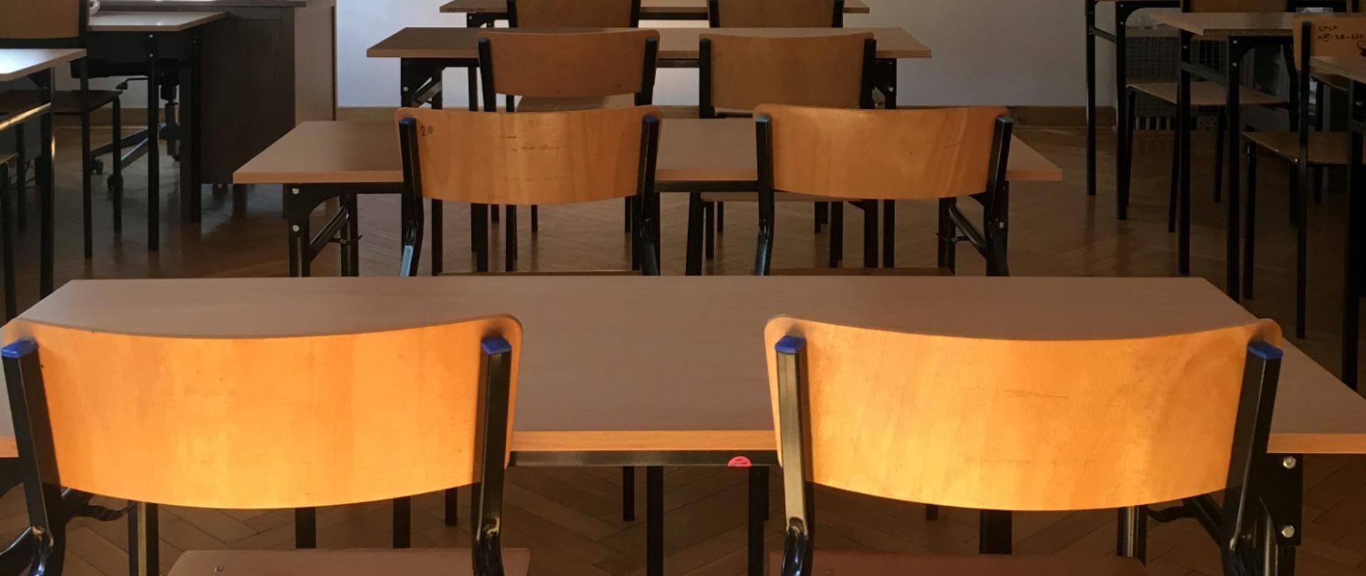 Pusta sala lekcyjna widziana z tylnej części, kadr obejmuje ławki szkolne.