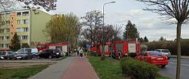Zdjęcie przedstawia samochody strażackie stojące przed budynkiem mieszkalnym wielorodzinnym. Samochody zaparkowane na parkingu oraz na ulicy Wyszyńskiego. 