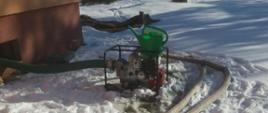 Na zdjęciu widoczna pompa szlamowa wypompowująca wodę z zalanej piwnicy, posesja ośnieżona, widoczne węże pożarnicze