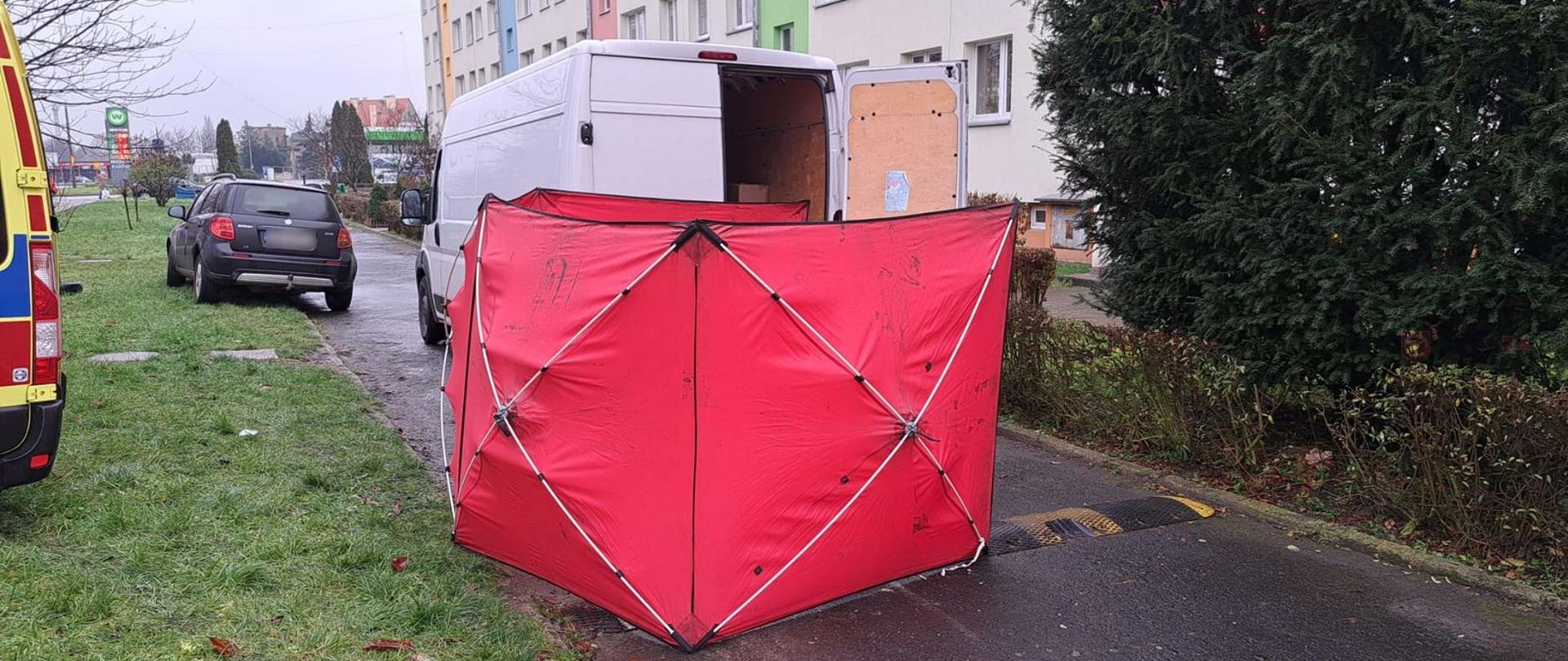 Śmiertelne potrącenie pieszego przy ul. Słowackiego w Brzegu - zdjęcie przedstawia czerwony parawan w tle biały samochód dostawczy oraz z lewej strony karetka pogotowia