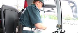 Kontrola autokaru turystycznego przed wyjazdem w podróż z dziećmi i młodzieżą. Inspektor mazowieckiej Inspekcji Transportu Drogowego pobiera wydruk i dane cyfrowe z tachografu pojazdu w celu kontroli czasu pracy kierowcy.