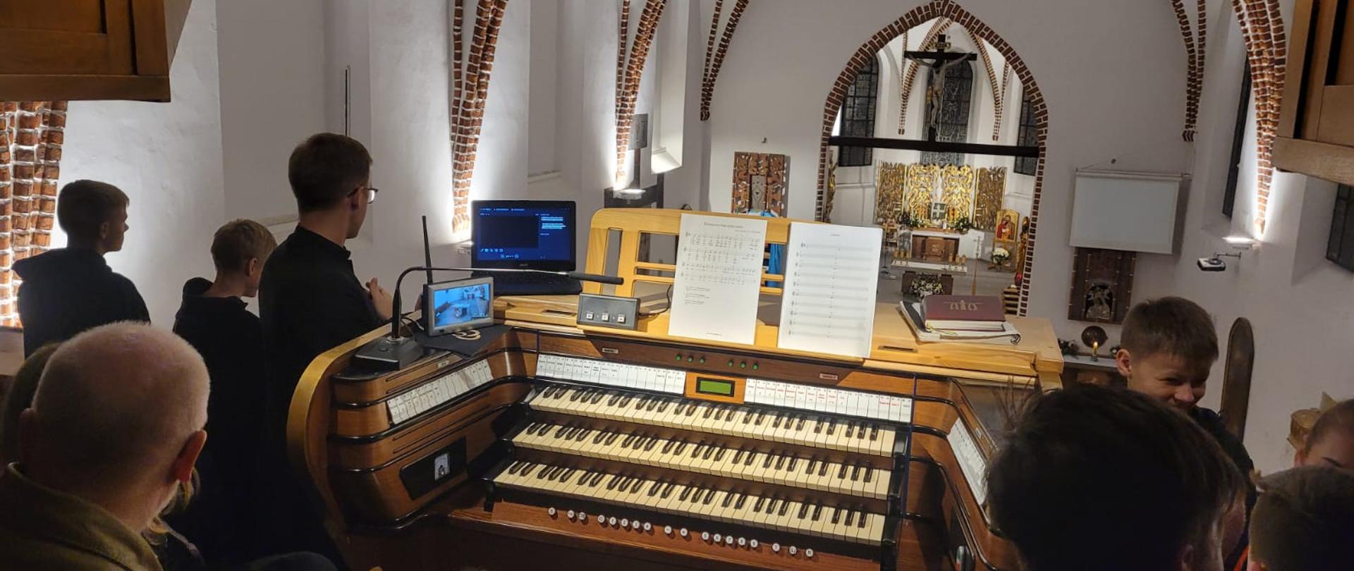 uczniowie i opiekunowie zabrani przy organach na chórze, w tle widok na kościół