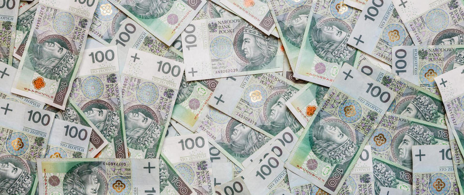 Chaotycznie rozrzucone banknoty o nominale 100 zł.