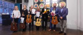 Czwórka uczennic trzymająca gitary z dyplomami wraz z trójką osób dorosłych pozujący do zdjęcia grupowego.