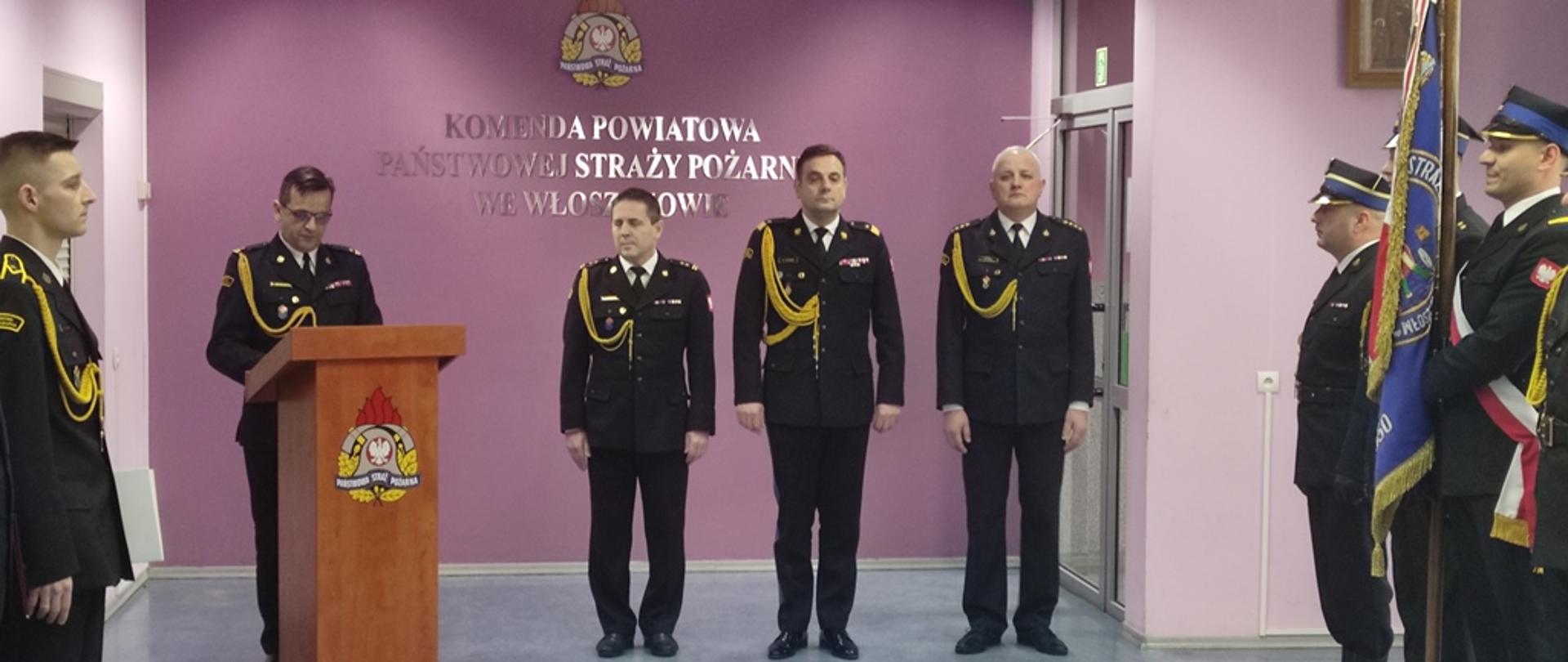 Sala Narad KP PSP we Włoszczowie, na środku ustawiona mównica, obok niej Świętokrzyski Komendant Wojewódzki PSP, zdający obowiązki zastępcy komendanta powiatowego PSP we Włoszczowie bryg. Zbigniew Starzyk, przyjmujący obowiązki zastępcy komendanta powiatowego PSP we Włoszczowie st. kpt. Andrzej Smal, przemawia komendant powiatowy PSP we Włoszczowie mł. bryg. Andrzej Pacanowski, po obu stronach Sali pracownicy komendy oraz zaproszeni goście
