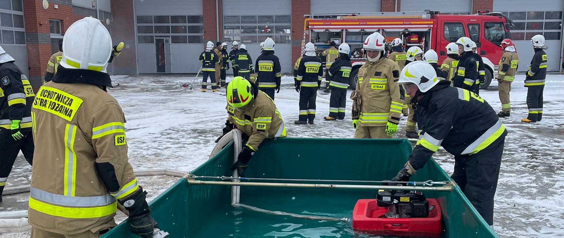 Strażacy podczas egzaminu praktycznego czerpią wodę ze zbiornika pompą pływającą