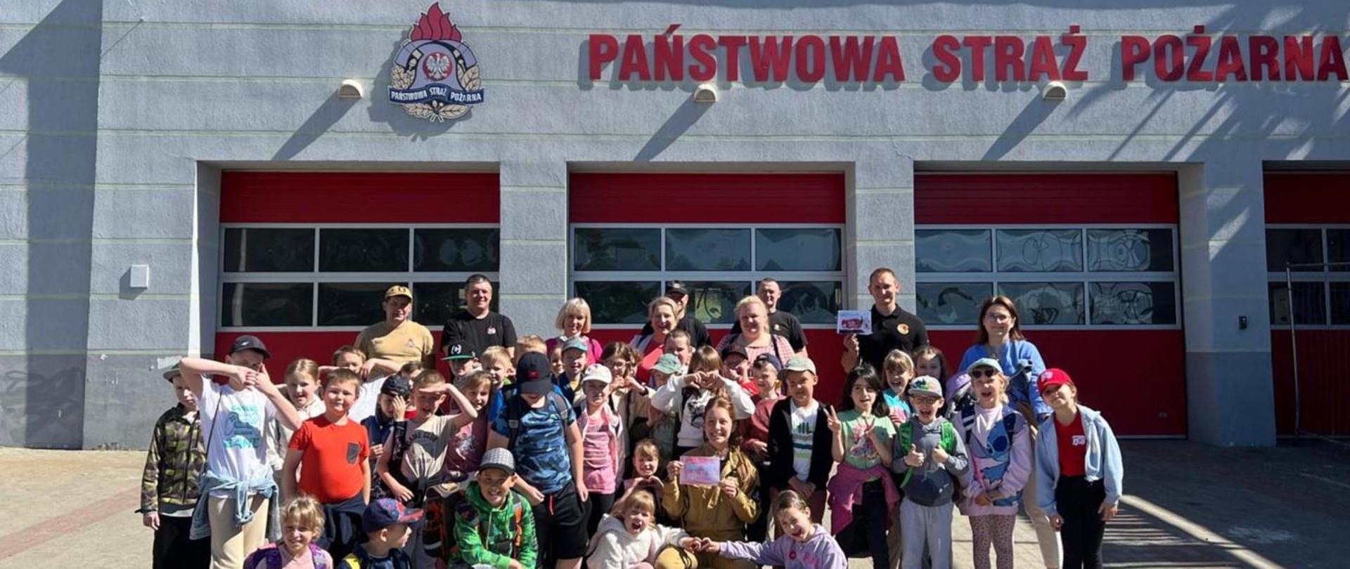 Zorganizowana grupa przedszkolna pozuje do zdjęcia z funkcjonariuszami na tle komendy.