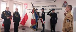 Nowy funkcjonariusz składa ślubowanie przed Komendantem Powiatowym i Zastępcą Komendanta Powiatowego PSP w Makowie Mazowieckim. Na wprost stoi poczet sztandarowy komendy. 
