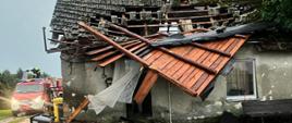 Na zdjęciu widac budynek z zerwanym dachem, w tle samochód pożarniczy