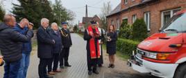 Zdjęcie przedstawia Ks. Józefa Oleskiego - Kapelana Powiatowy Strażaków podczas poświęcenia lekkiego samochodu ratowniczo – gaśniczego. Na zdjęciu widać między innymi Pana Mariusza Łuczyk - Wicewojewodę Pomorskiego, Pana Aleksandra Mrówczyńskiego - poseła na Sejm Rzeczypospolitej Polskiej, bryg. Wojciecha Berent - Zastępcę Pomorskiego Komendanta Wojewódzkiego PSP. Po lewej Samochód pożarniczy.