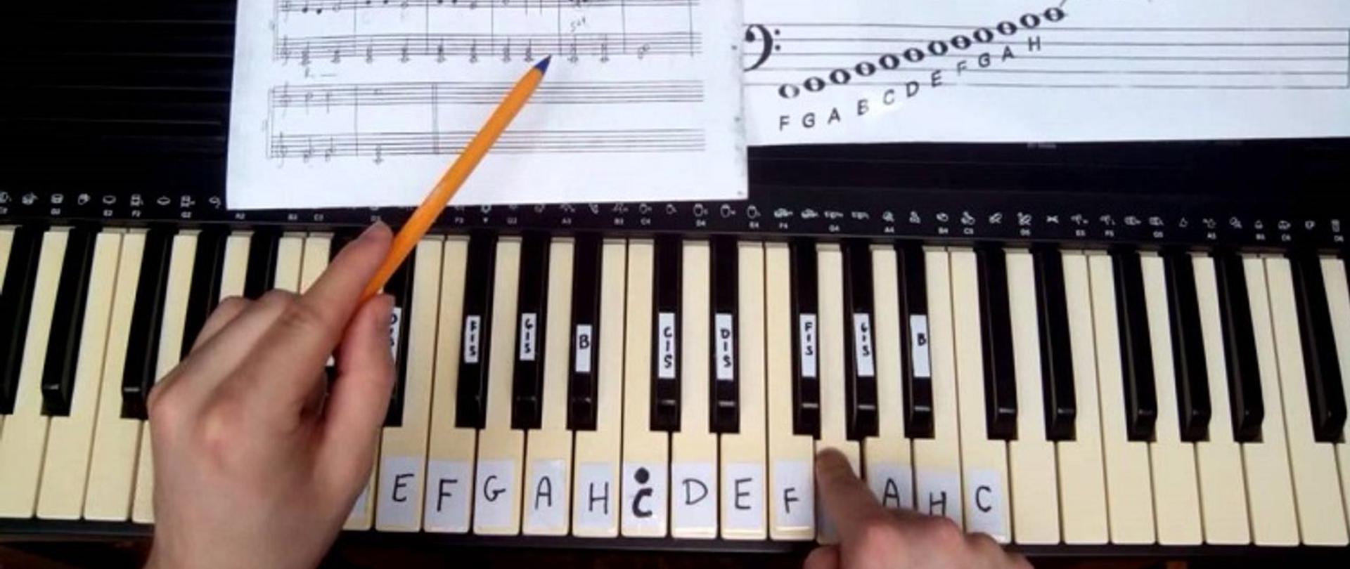 Na zdjęciu przedstawione są klawisze pianina, długopis oraz zeszyt z nutami