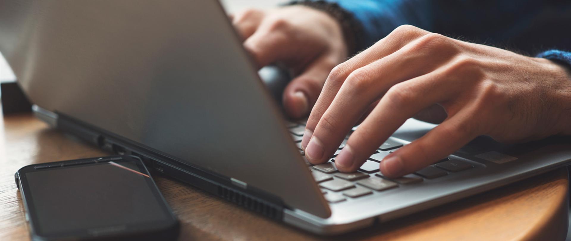 Dłonie na klawiaturze laptopa, telefon komórkowy.