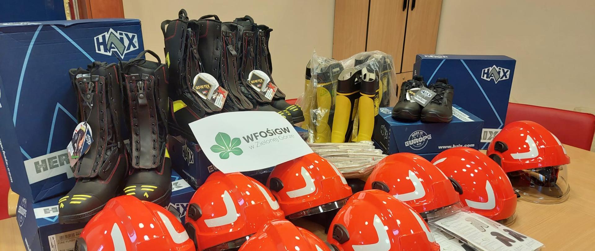 Zdjęcie przedstawia pozyskany sprzęt w ramach programu - Doposażenie Komendy Powiatowej Państwowej Straży Pożarnej w środki ochrony indywidualnej dla ratowników biorących udział w działaniach ratowniczo - gaśniczych. Głównie widać hełmy oraz buty specjalne.