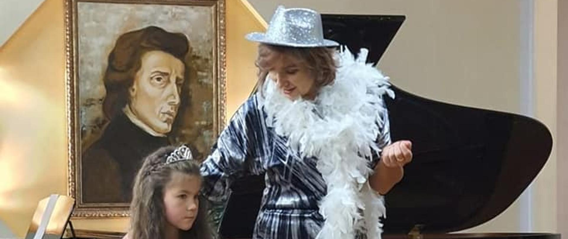 Zdjęcie przedstawia uczennicę wraz z nauczycielem P. Joanna Kocyan. Zdjęcie wykonane podczas koncertu karnawałowego dla uczniów - 12 stycznia 2023 w auli PSM I st. w Kłodzku, w tle widoczny fortepian.