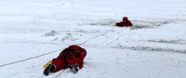 Strażak czołgając się po tafli lodu zbliża się do innego strażaka znajdującego się przeręblu celem podjęcia go z wody.