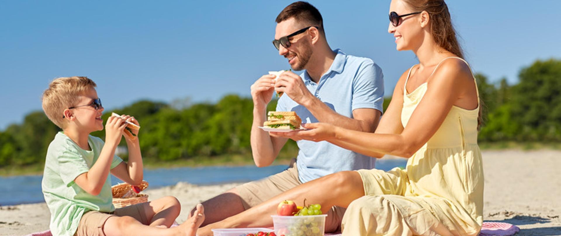 rodzina na kocu na plaży spożywa posiłek