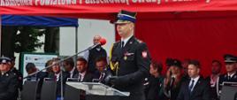 Powiatowe Obchody Dnia Strażaka w Siemiatyczach - st. bryg. Marcin Wierel przemawia, w tle zaproszeni goście siedzą na krzesełkach pod namiotem PSP
