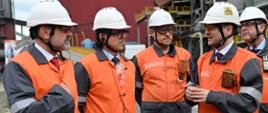 Minister Wojciech Balczun, wiceminister Grzegorz Wrona i przedstawiciele ArcelorMittal Poland w pomarańczowych strojach i kaskach.