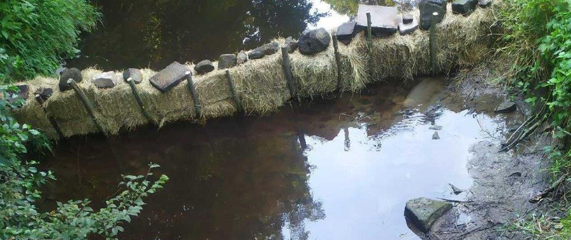 Zapora z bali słomy na rzece