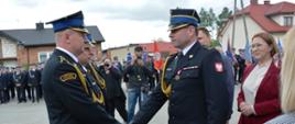 Strażacy w mundurach wyjściowych. Na pierwszym planie Zastępca Łódzkiego Komendanta Wojewódzkiego gratuluje strażakowi. 