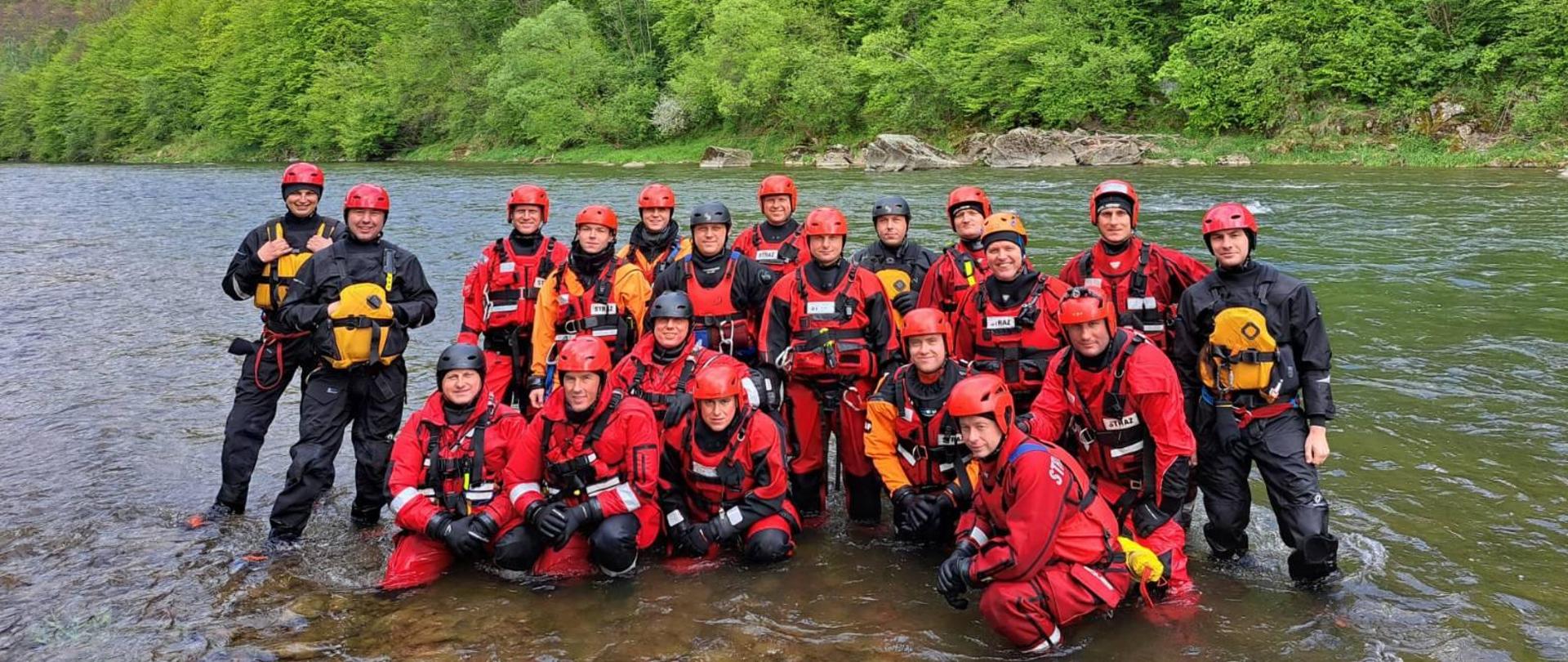 Szkolenie strażaka Komendy Powiatowej PSP w Sokołowie Podlaskim z zakresu ratownictwa na wodach szybkopłynących - wspólne zdjęcie w rzece, w tle zadrzewiony brzeg