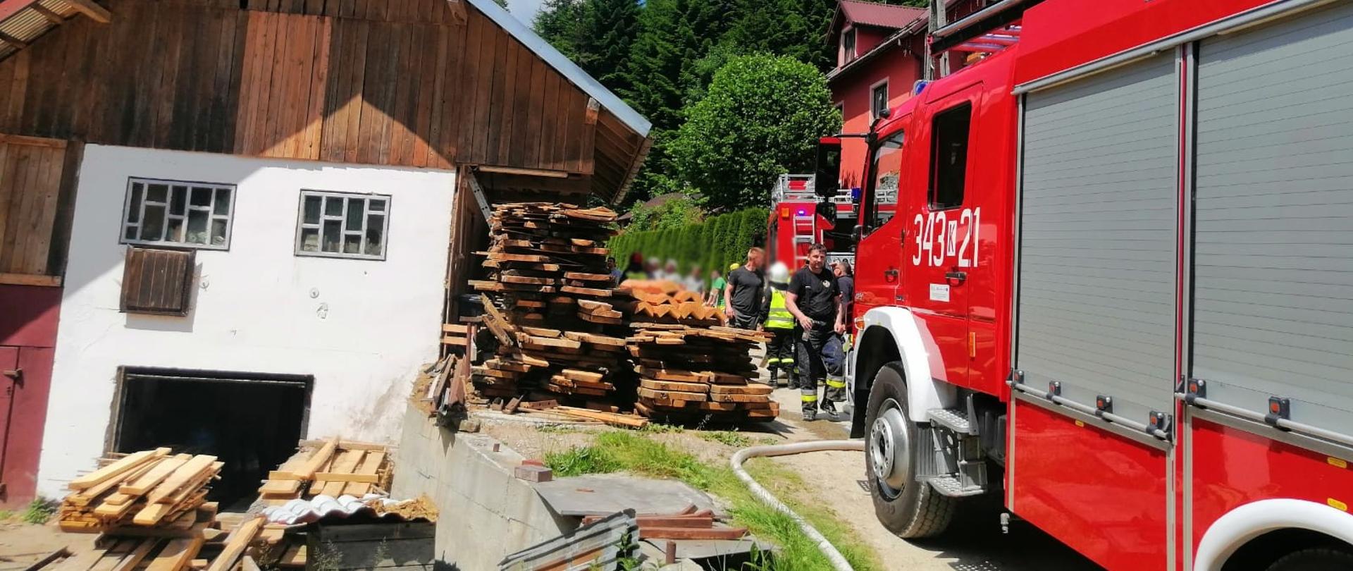 Samochód pożarniczy oraz strażacy przed budynkiem stolarni.