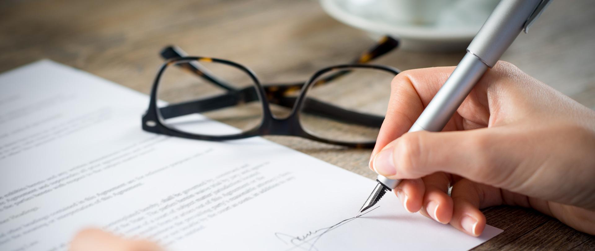 Closeup shot of a woman signing a form. She's writing on a financial contract. Shallow depth of field with focus on tip of the pen.
