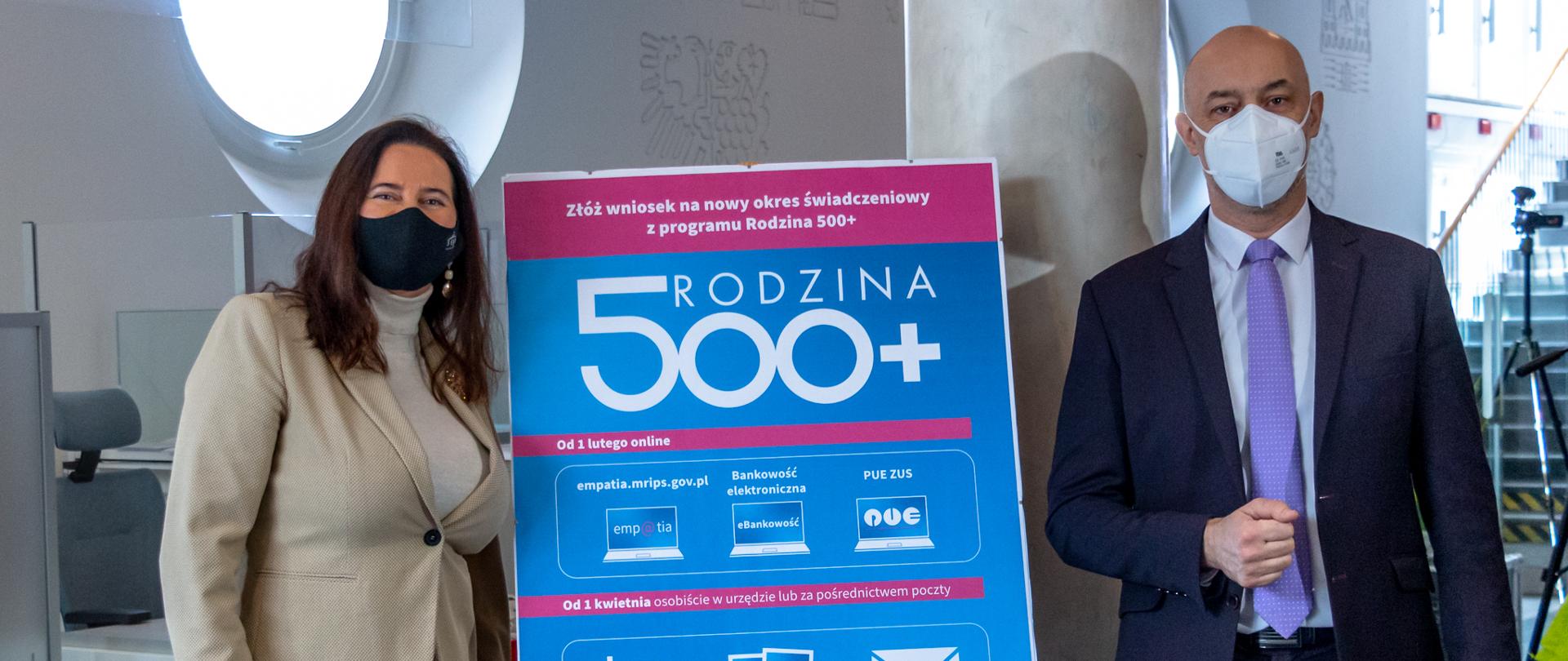 Wojewoda opolski Adrian Czubak stoi po prawej stronie kadru, poseł na Sejm RP Violetta Porowska po lewej. Pomiędzy nimi widać sztalugę, na której ustawiono duży plakat informacyjny dotyczący realizacji Programu Rodzina 500 plus. Na błękitnym plakacie widać infografiki, m.in. kopertę, zarys druku, domu oraz trzy grafiki, prezentujące ekran komputera. Infografiki wyjaśniają jak poprawnie złożyć nowy wniosek do programu Rodzina 500 plus.
Wojewoda oraz poseł mają na twarzach maseczki ochronne. W tle widać korytarz urzędu.
