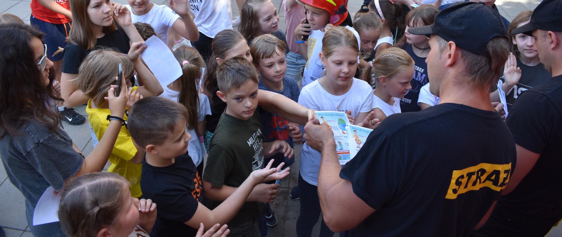 Strażak rozdaje broszury grupie dzieci i młodzieży.