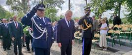 Mężczyzna w garniturze oraz przedstawiciele Policji oraz Państwowej Straży Pożarnej oddają honory.