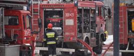 Na zdjęciu widać trzy samochody pożarniczej oraz strażaka obsługującego autopompę